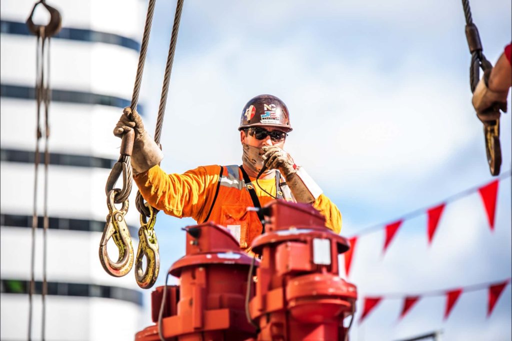 Man wearing safety glasses and orange shirt holding crane hook | Crane Services | NessCampbell