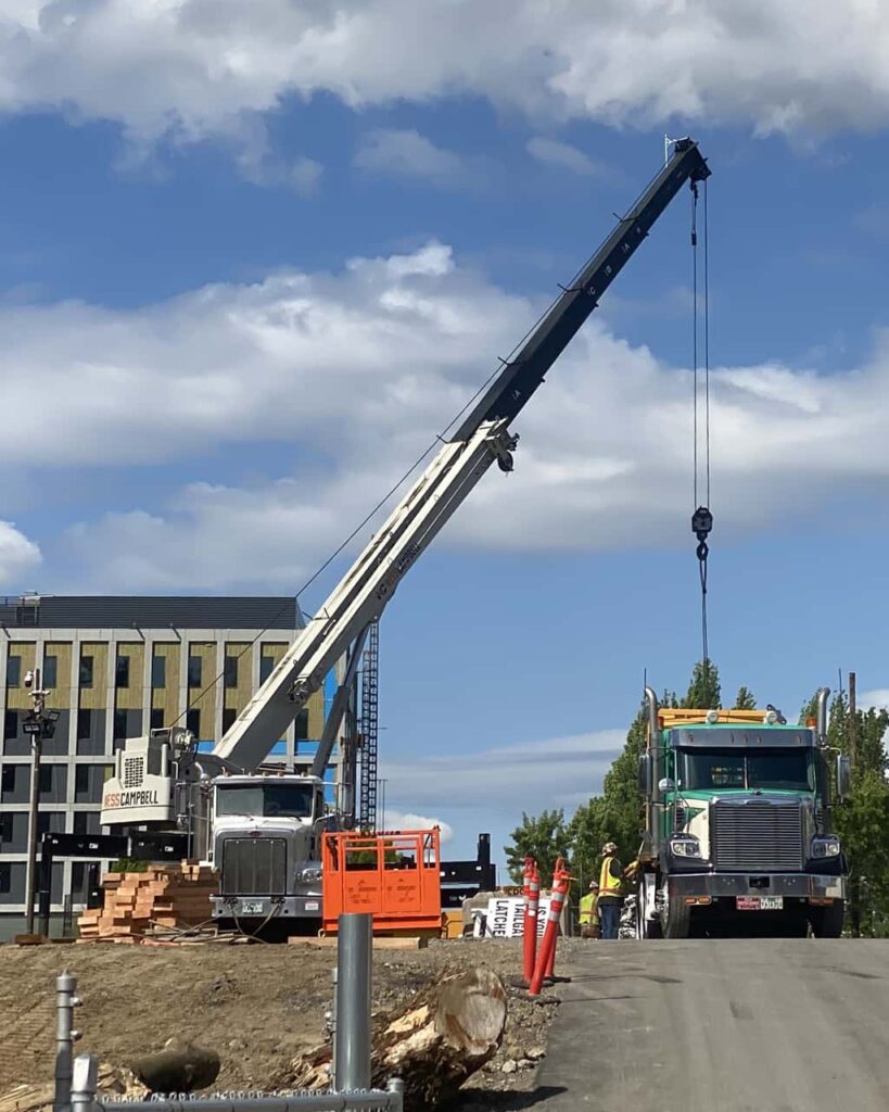 A crane hoists a sizable object onto a big truck | Crane Rental Services | NessCampbell
