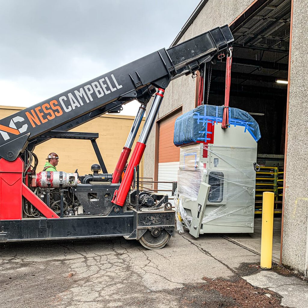 A crane hoisting a big machine into a warehouse | Crane Rental Services | NessCampbell